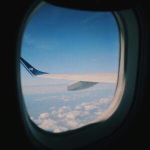 A serene view of sky and clouds through an airplane window, showcasing the aircraft wing.