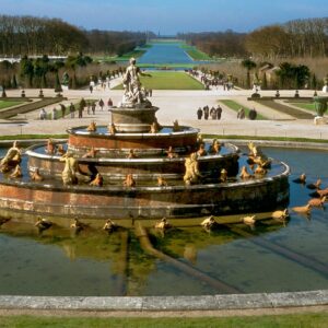 Classic fountain in the Gardens of Versailles surrounded by lush greenery and pathways.